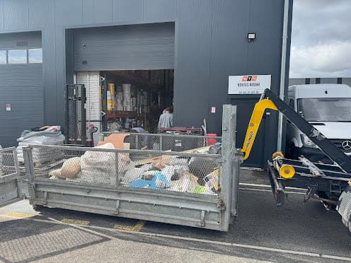 Benne à ridelles remplie d'encombrants et de cartons devant l'entrée d'un local professionnel