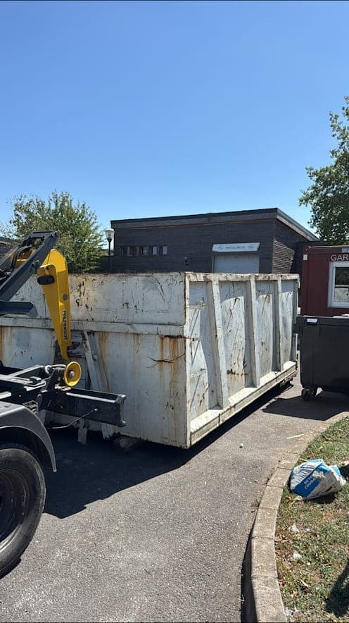 Grande benne métallique déposée par un camion ampliroll devant un bâtiment d'activité en briques